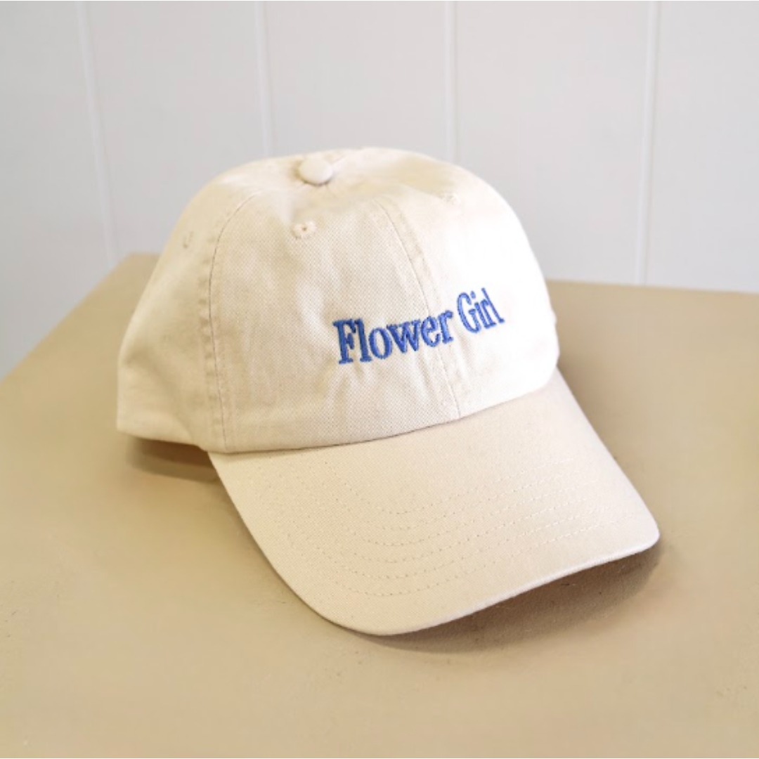 A beige baseball cap with blue embroidered text reading 'Flower Girl.' Same-day delivery Perth.